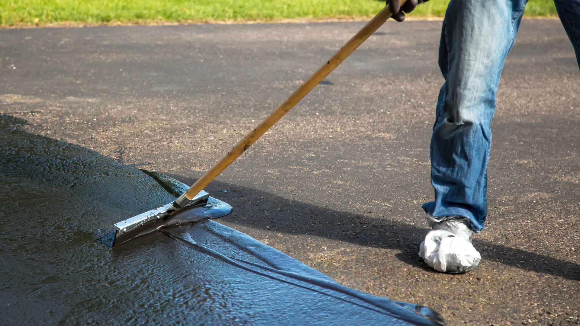 A person is using a broom to spread asphalt on a driveway.