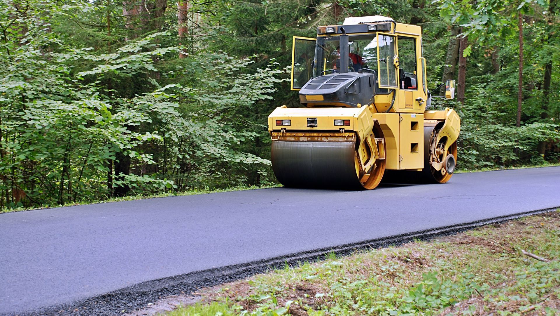 A yellow roller is driving down a road in the woods.