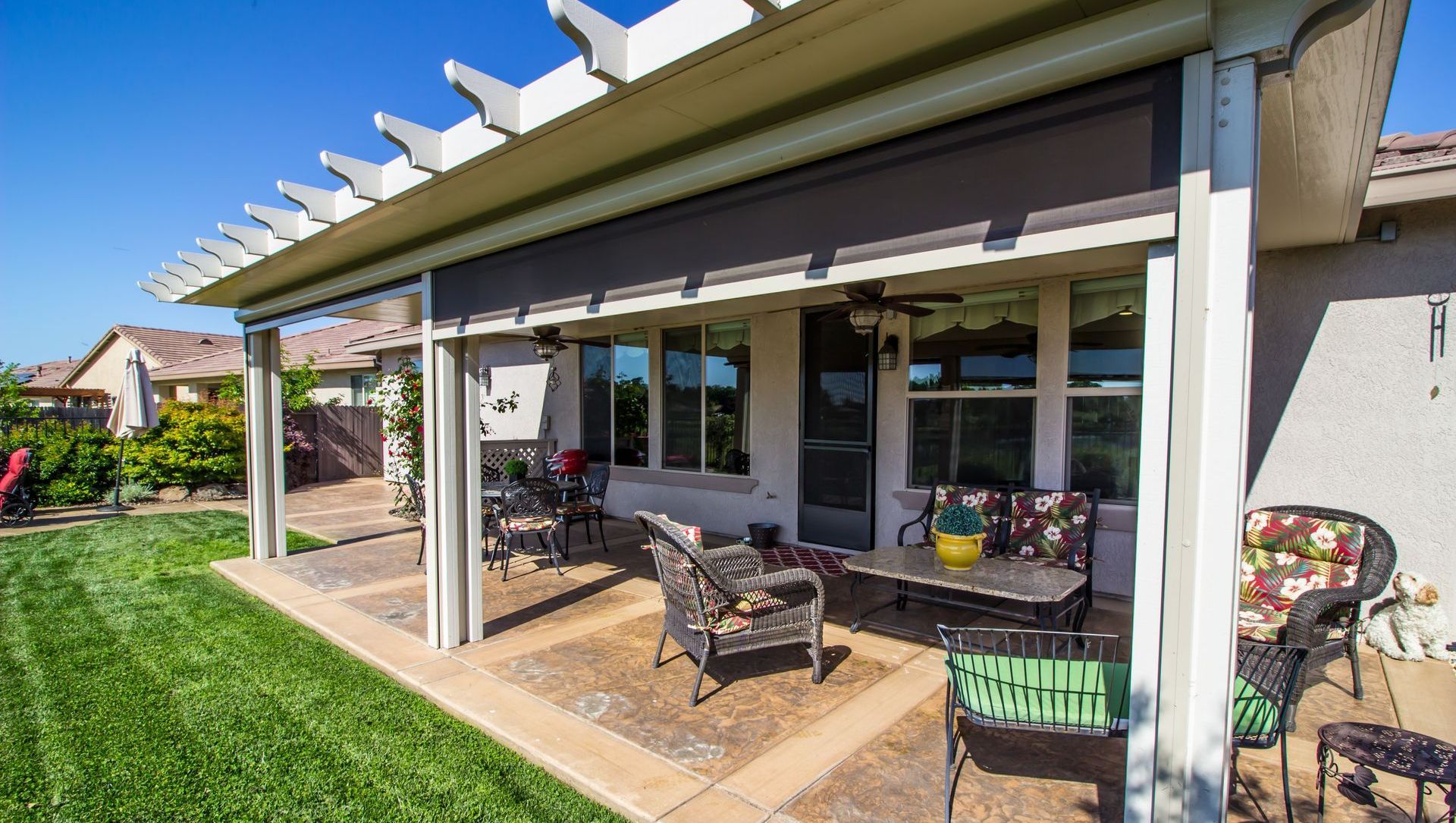 A patio with a pergola and a table and chairs in front of a house.