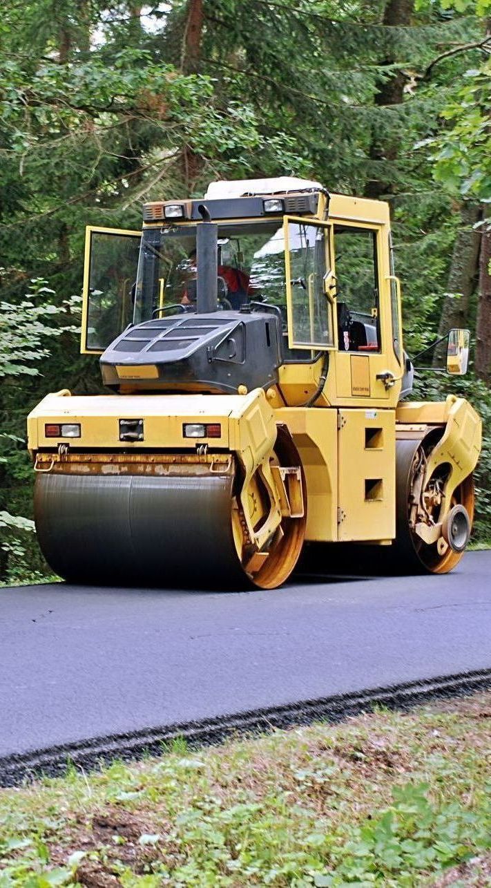 A yellow road roller is driving down a road.