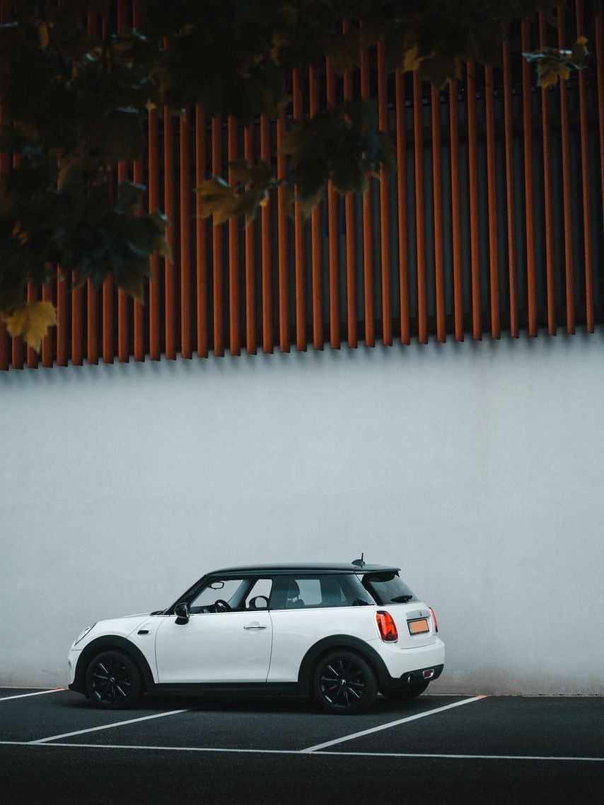 A white car is parked in a parking lot in front of a white wall.