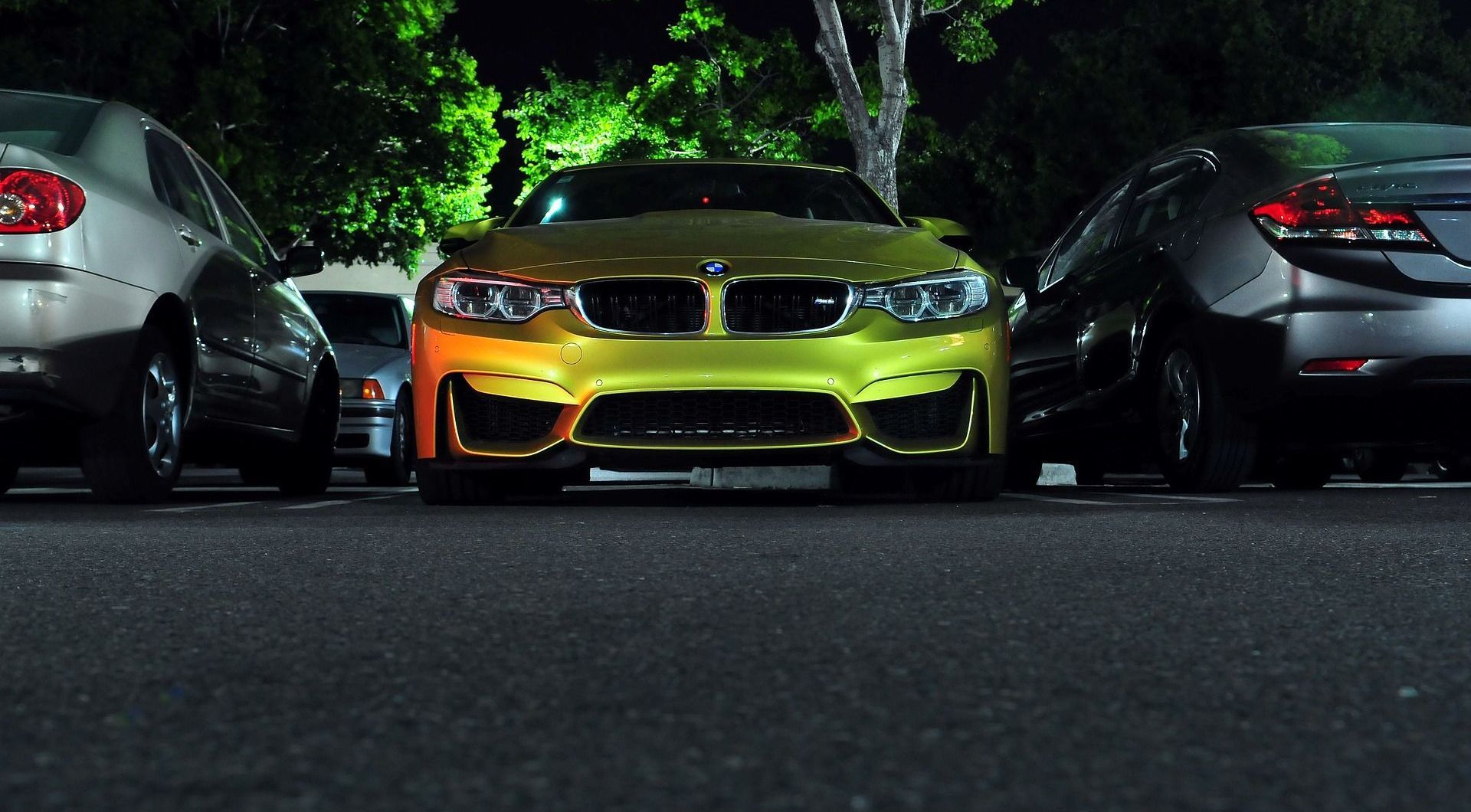 A yellow bmw is parked next to a silver car in a parking lot.