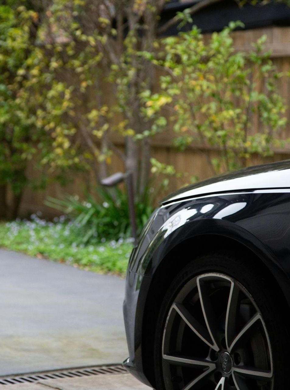 A black car is parked in a driveway with trees in the background.