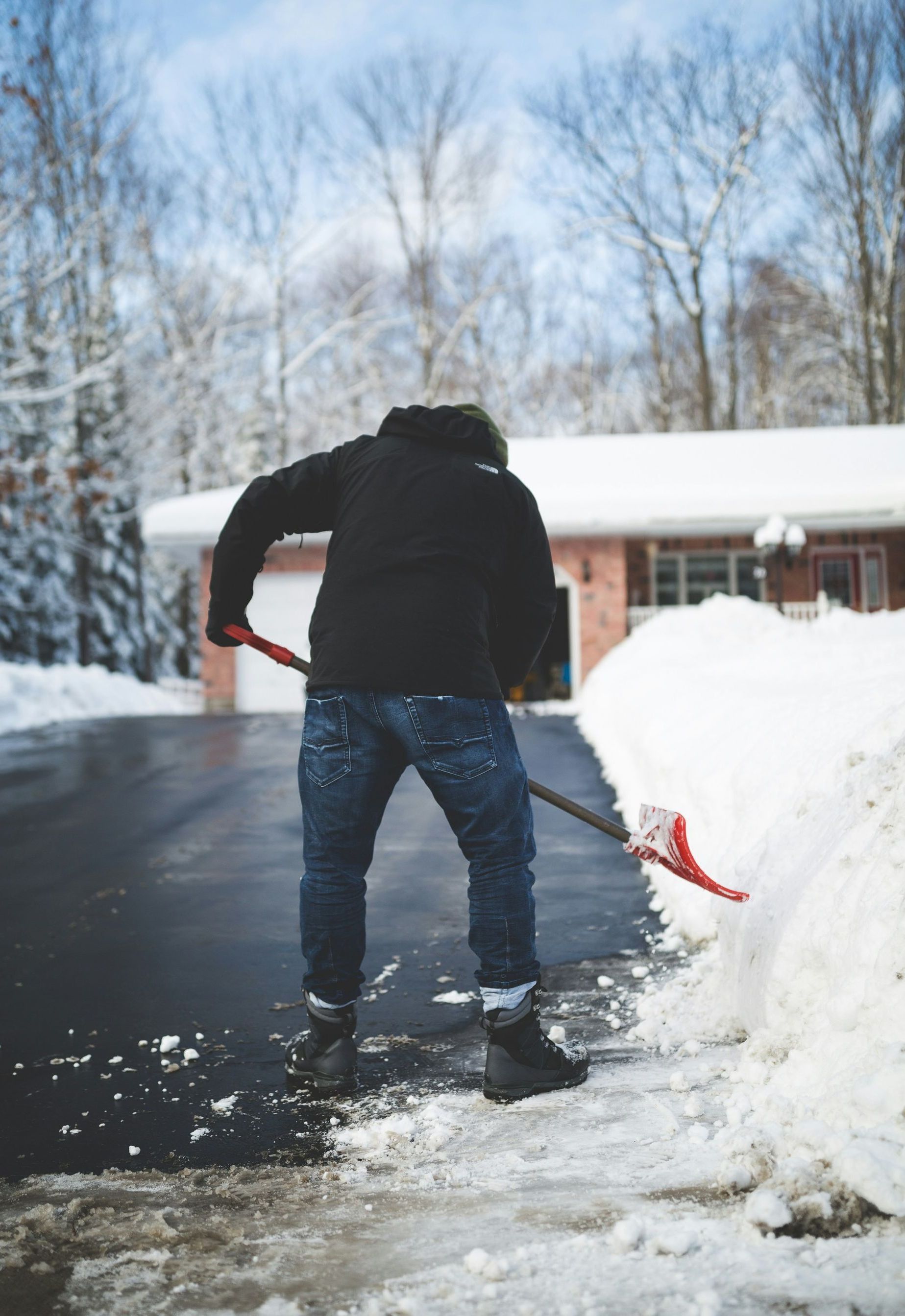 A man is shoveling snow from a driveway in front of a house.