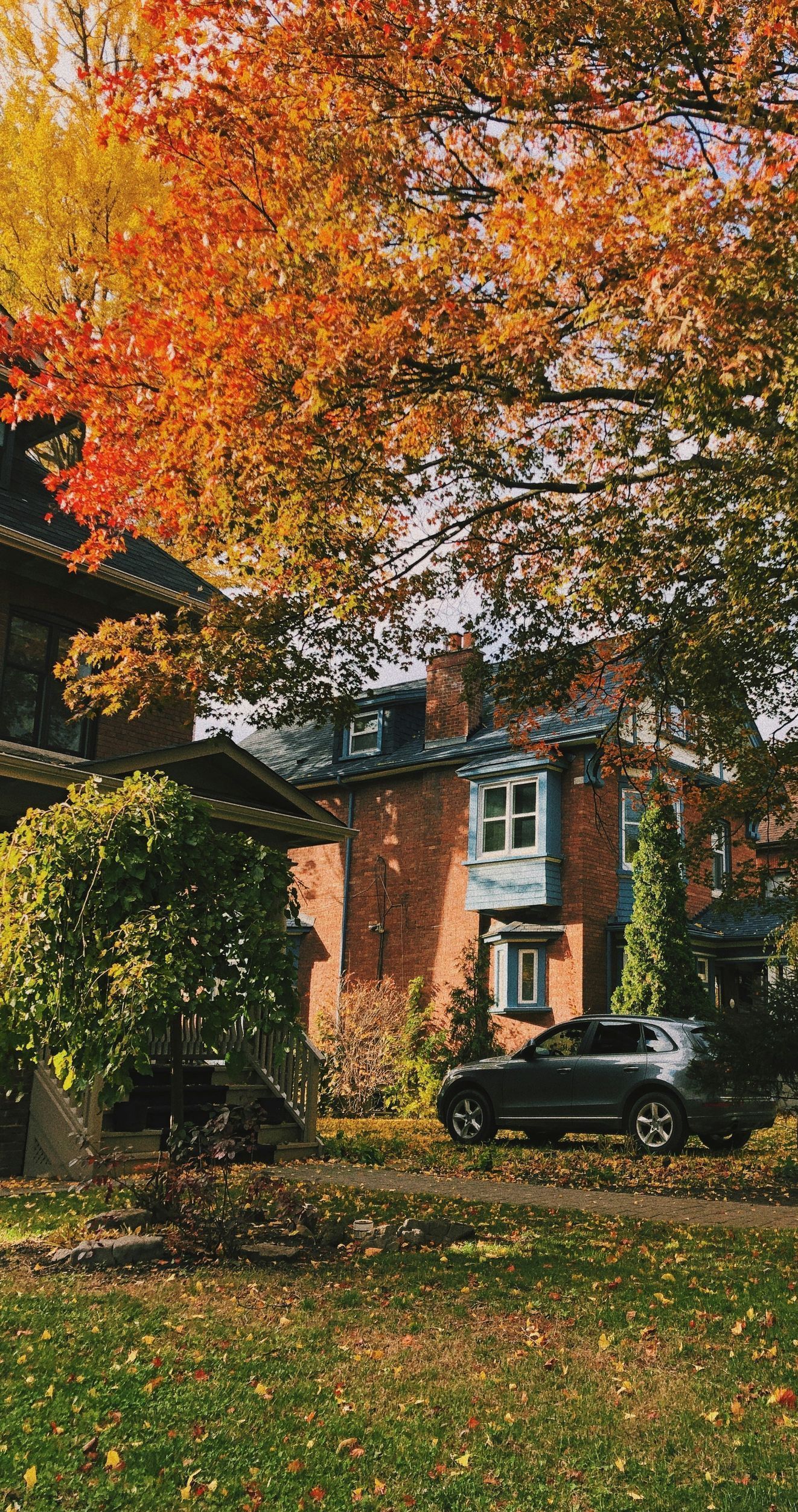 A car is parked in front of a house with trees in the background.