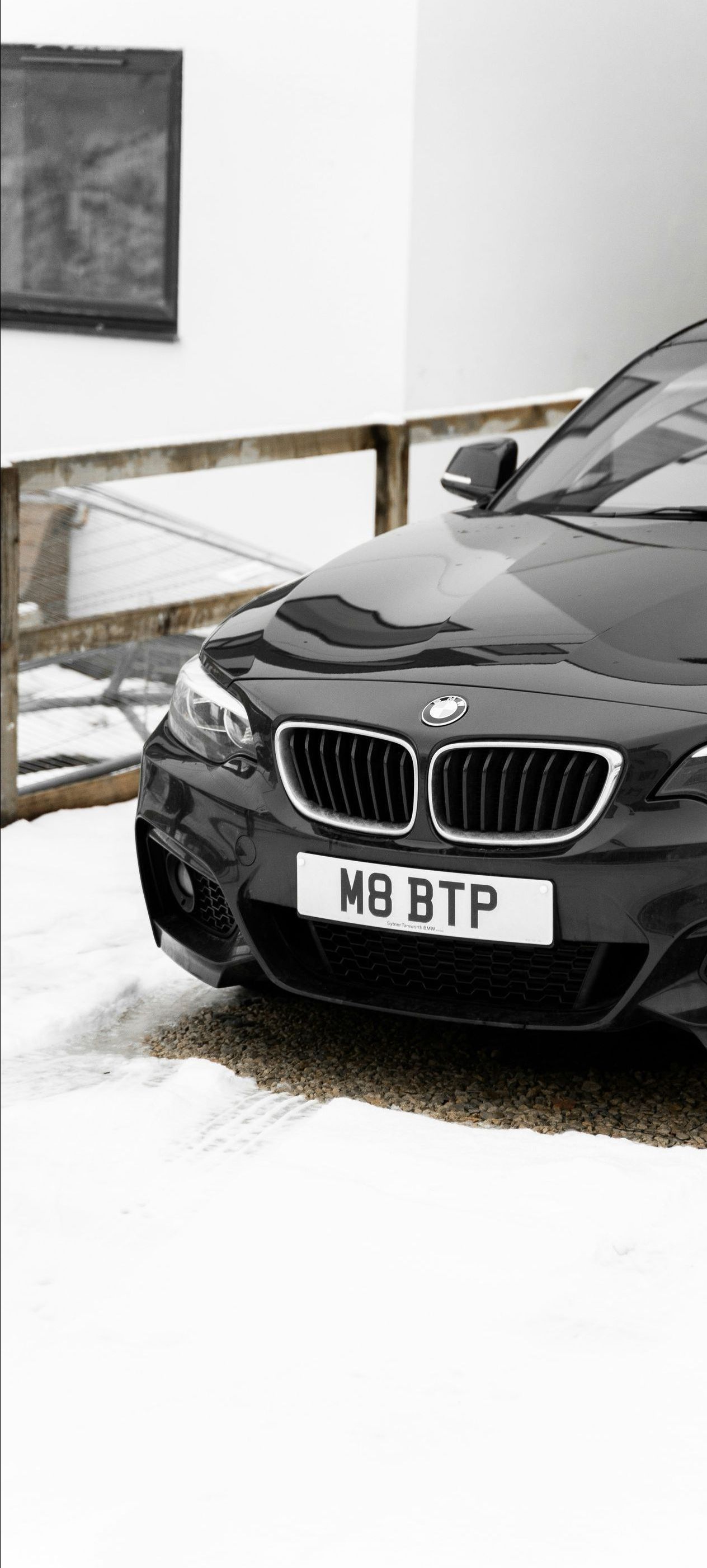 A black bmw is parked in the snow in front of a building.