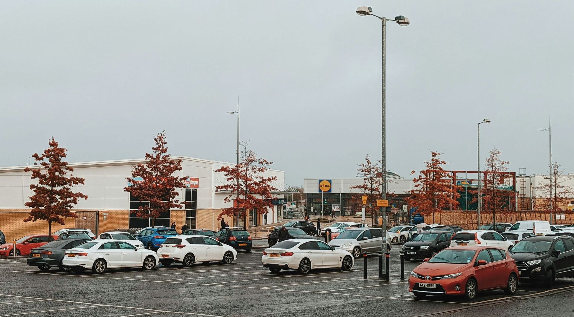 A lot of cars are parked in a parking lot in the rain.