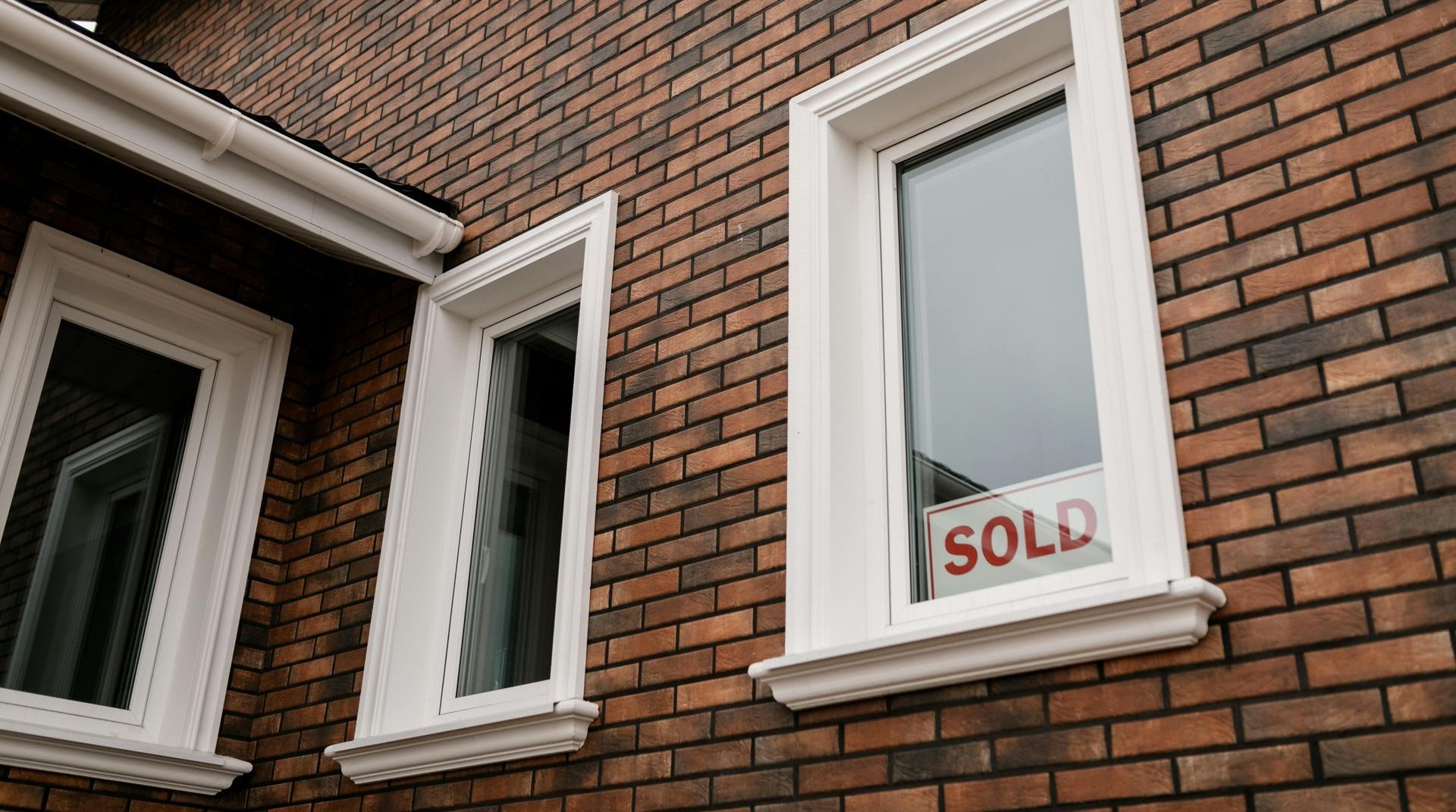 A brick house with a sold sign in the window.