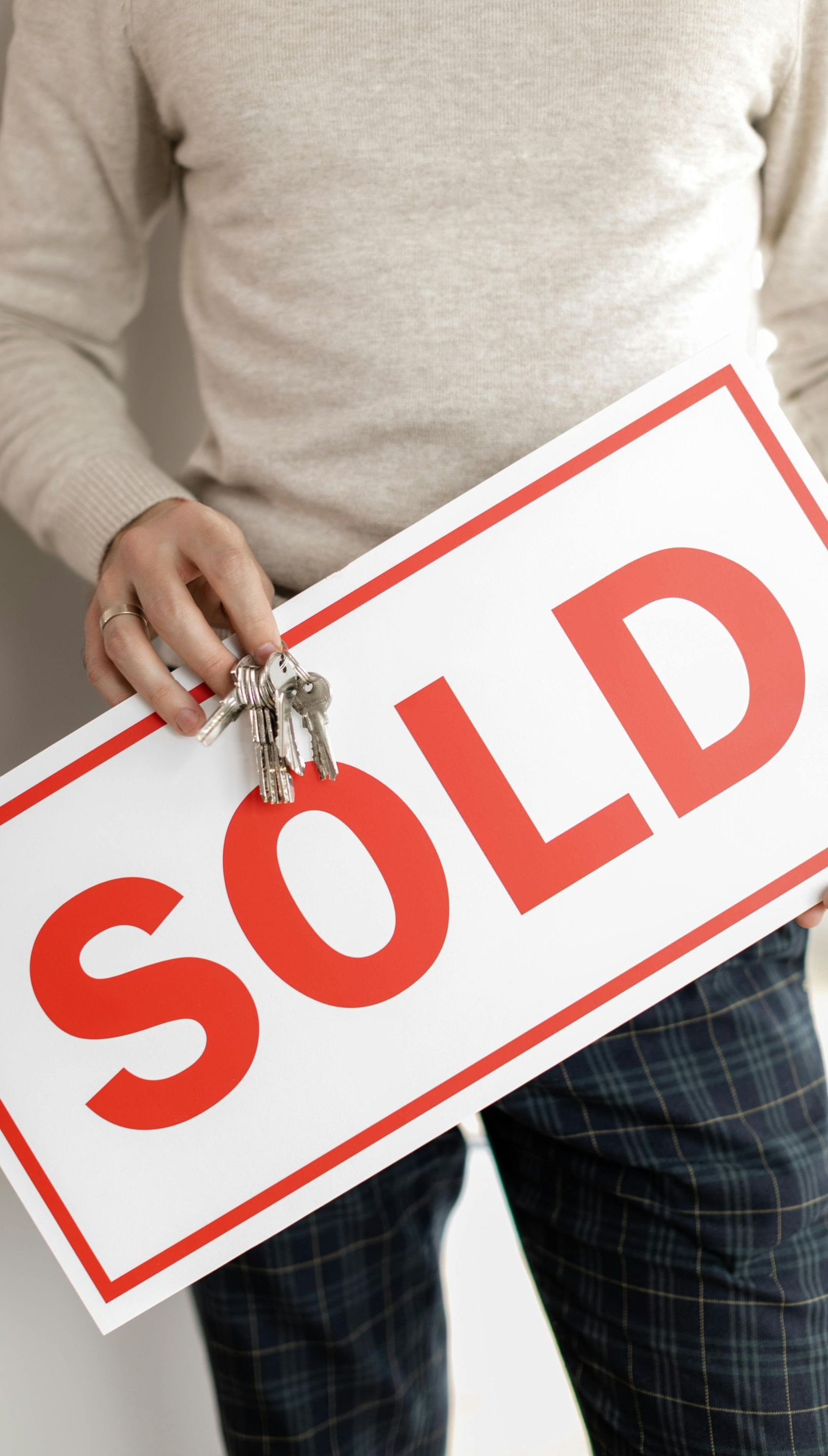 A man is holding a sold sign and keys.