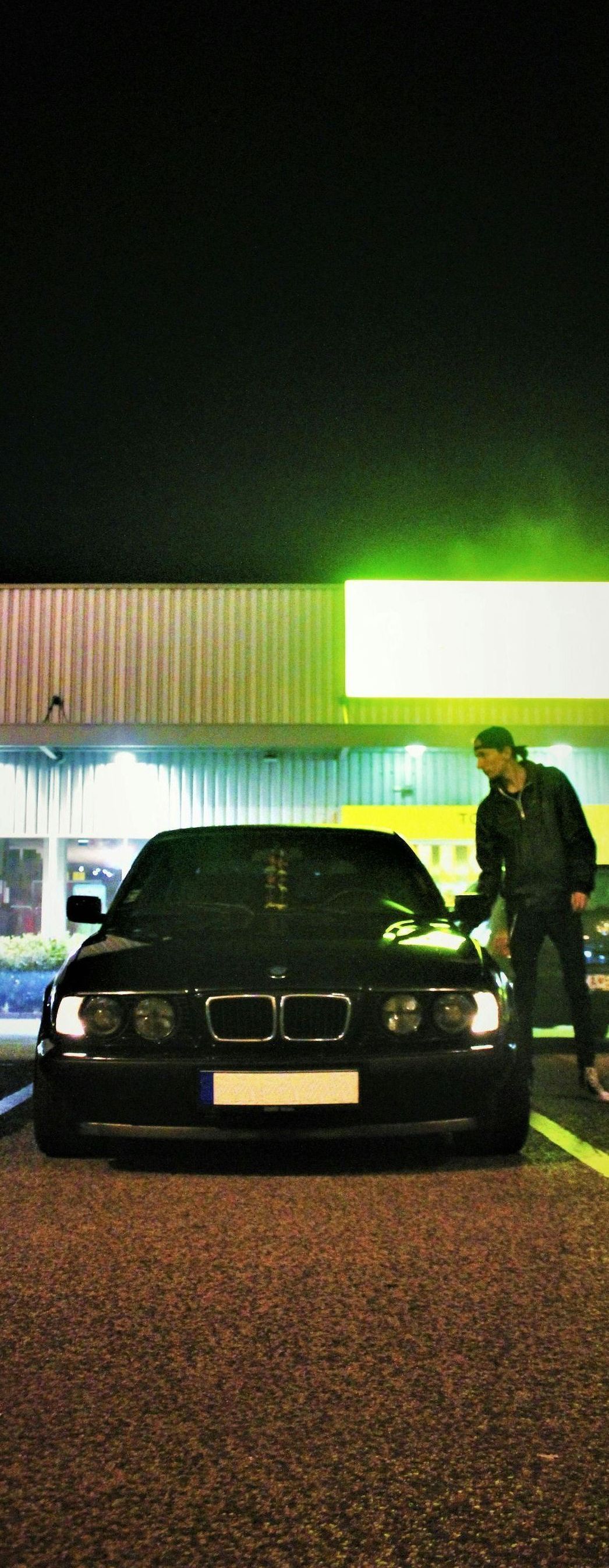 A man is standing next to a black car in a parking lot at night.