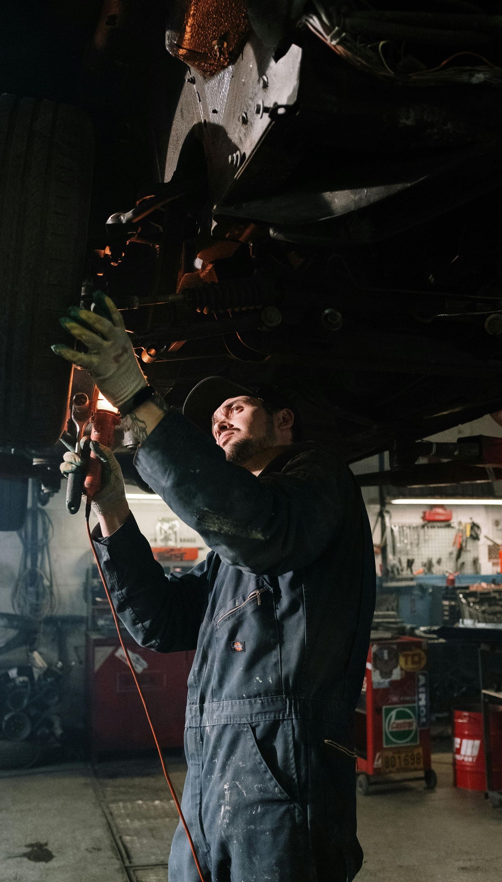 A man in overalls is working under a car in a garage.