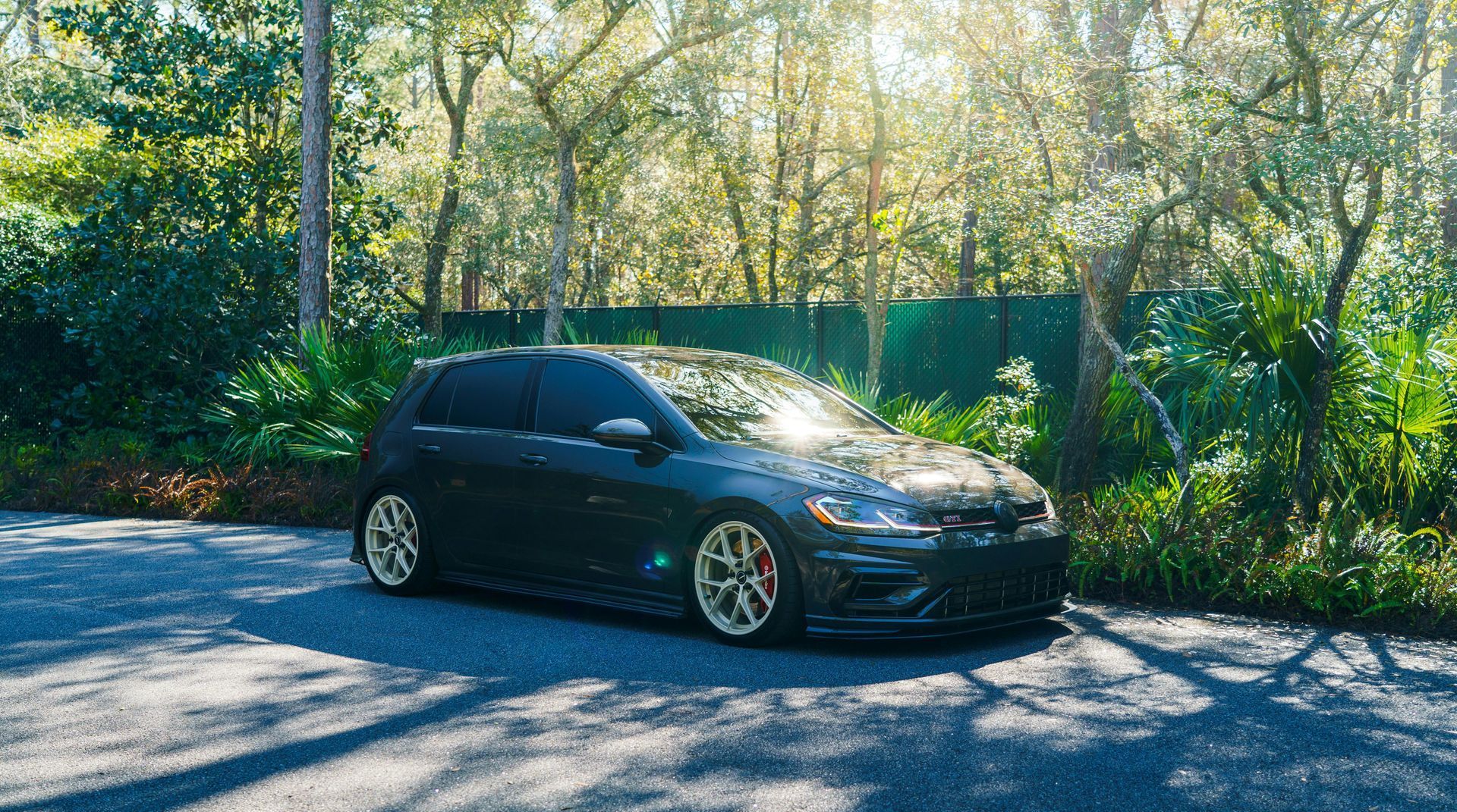 A black car is parked on the side of the road in front of a forest.