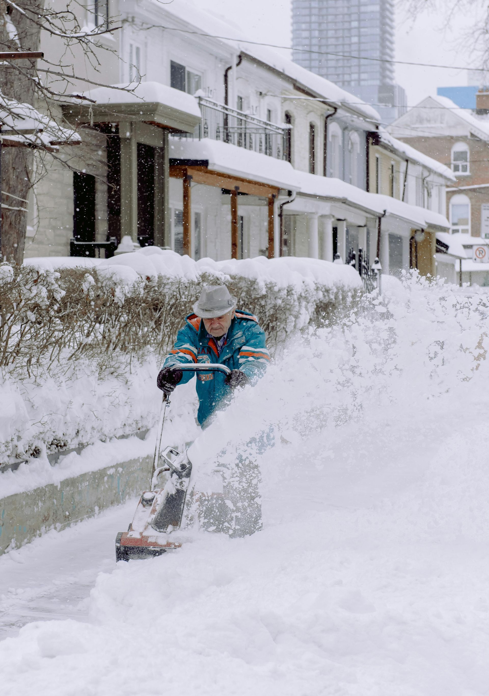 A man is blowing snow off the sidewalk with a snow blower.