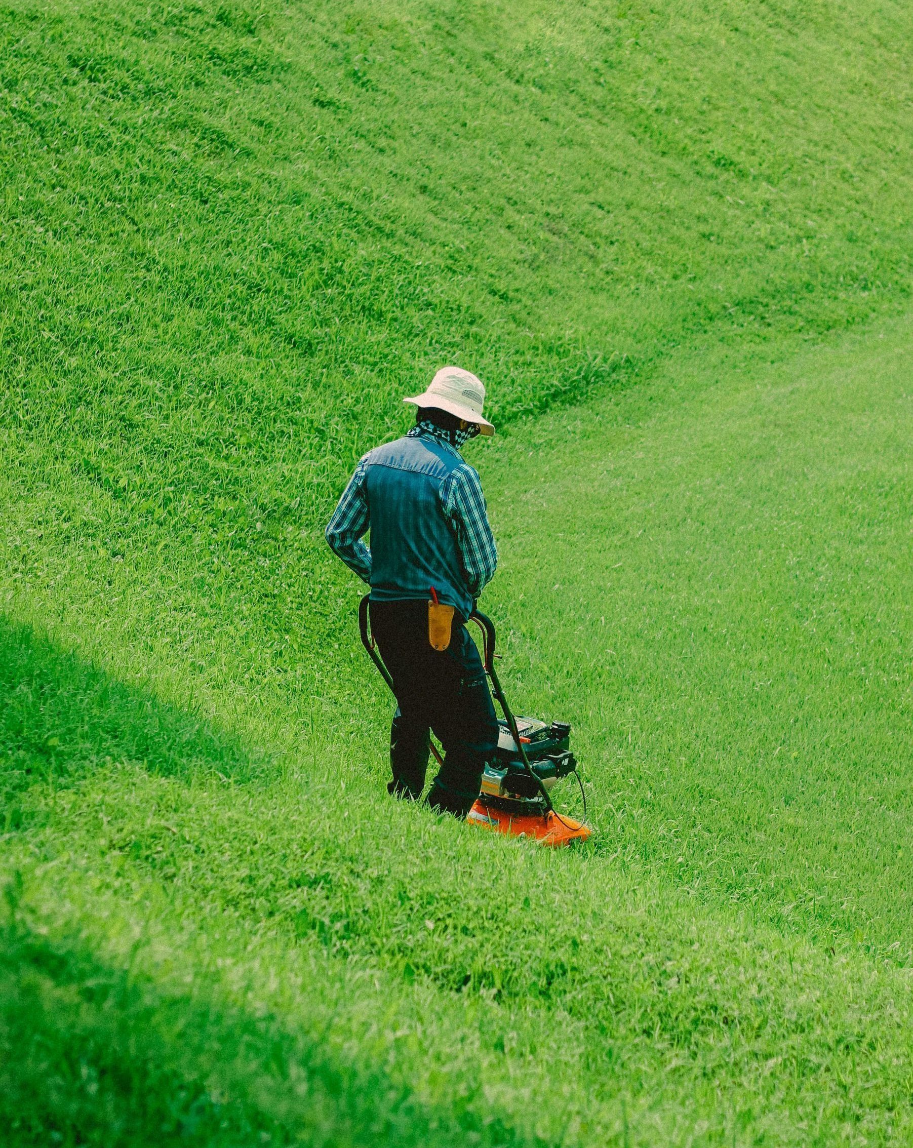 A man is mowing a lush green field with a lawn mower.