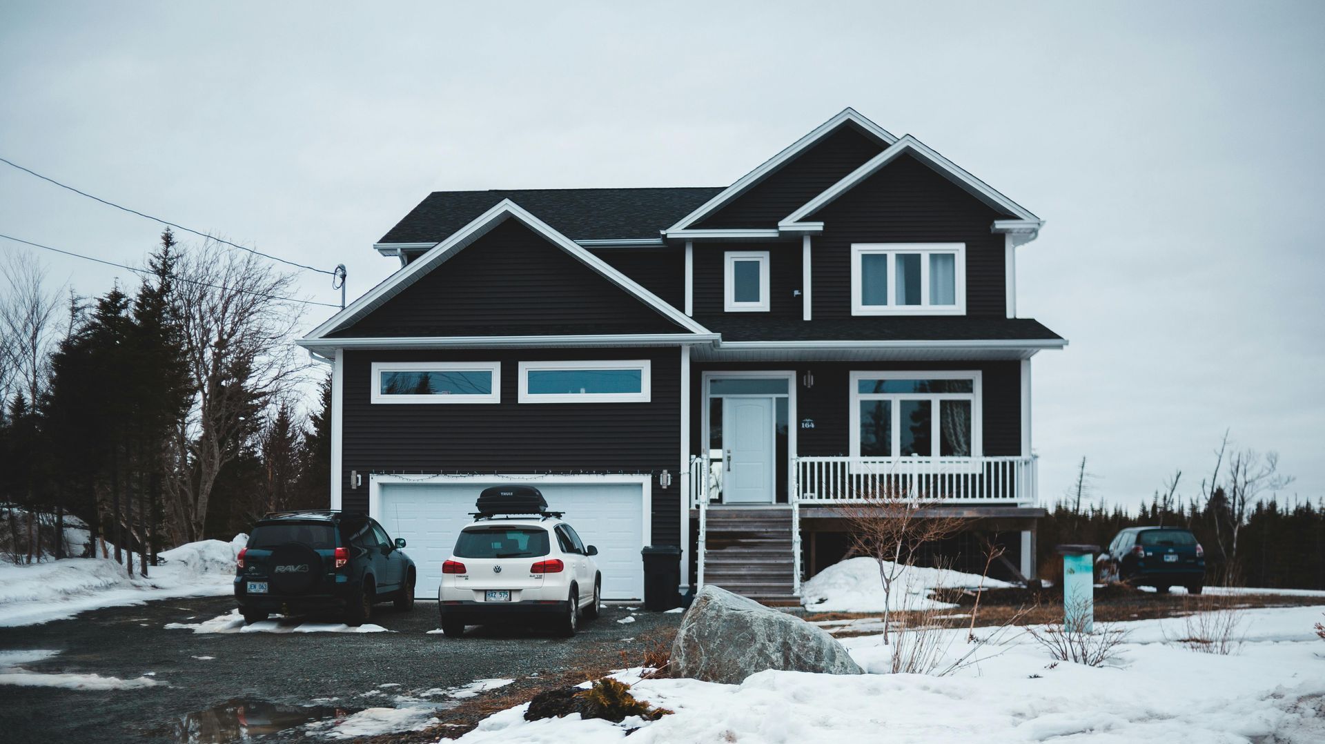 A black house with a white car parked in front of it