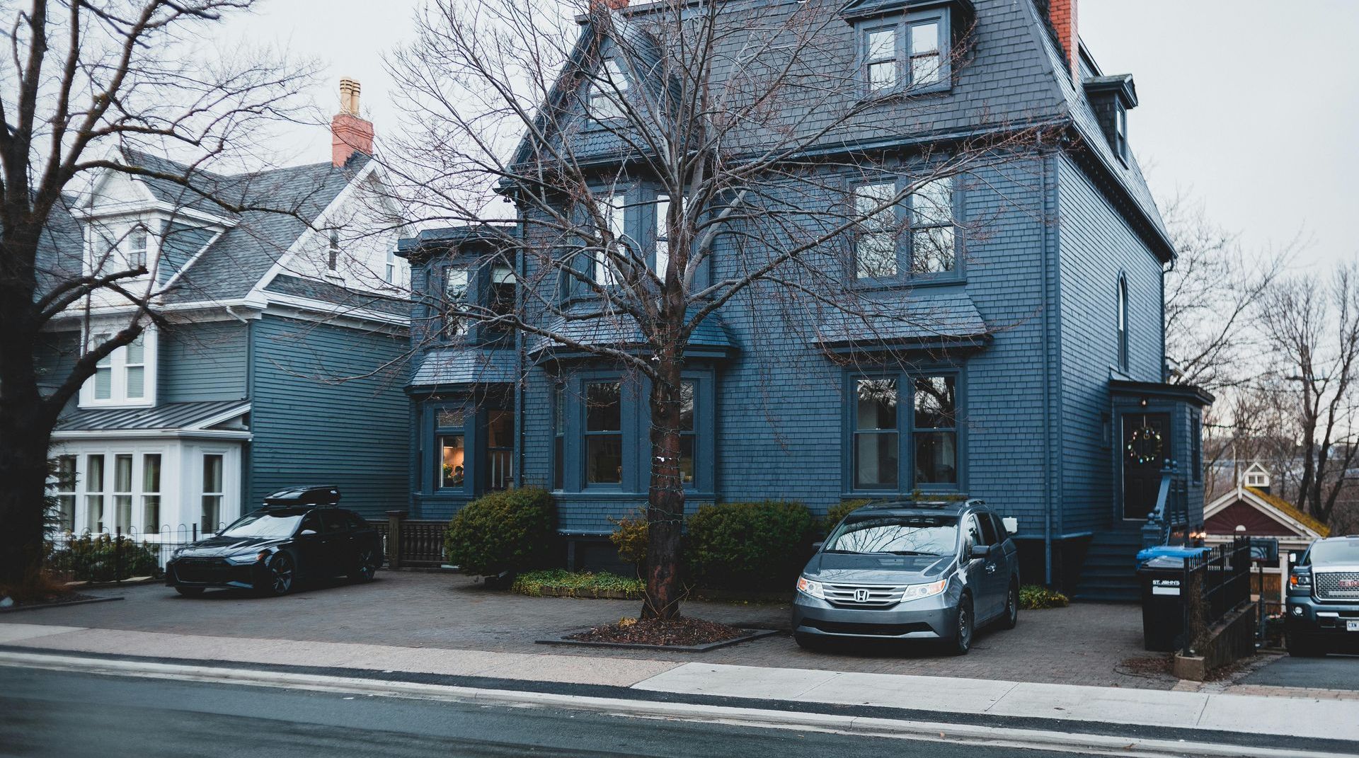 A blue house with cars parked in front of it on a rainy day.