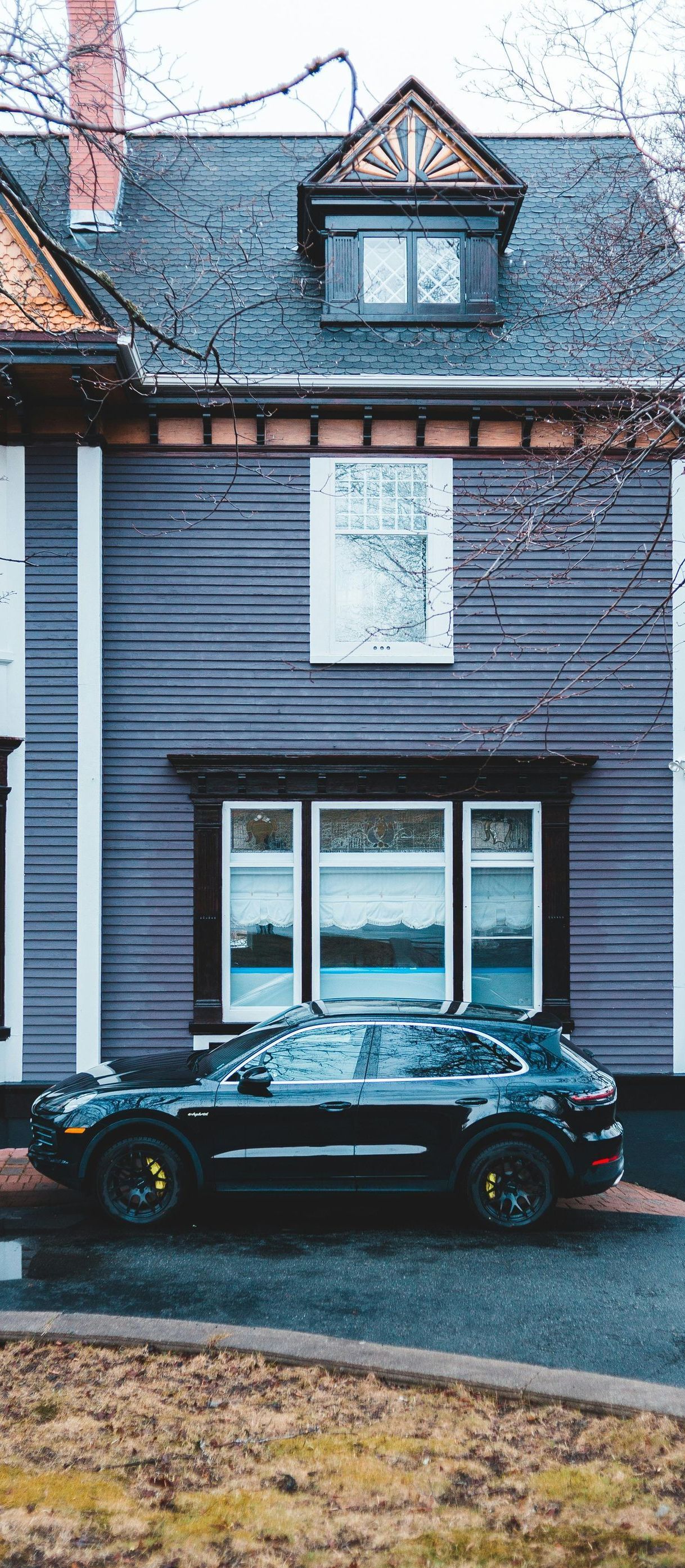 A black car is parked in front of a gray house.