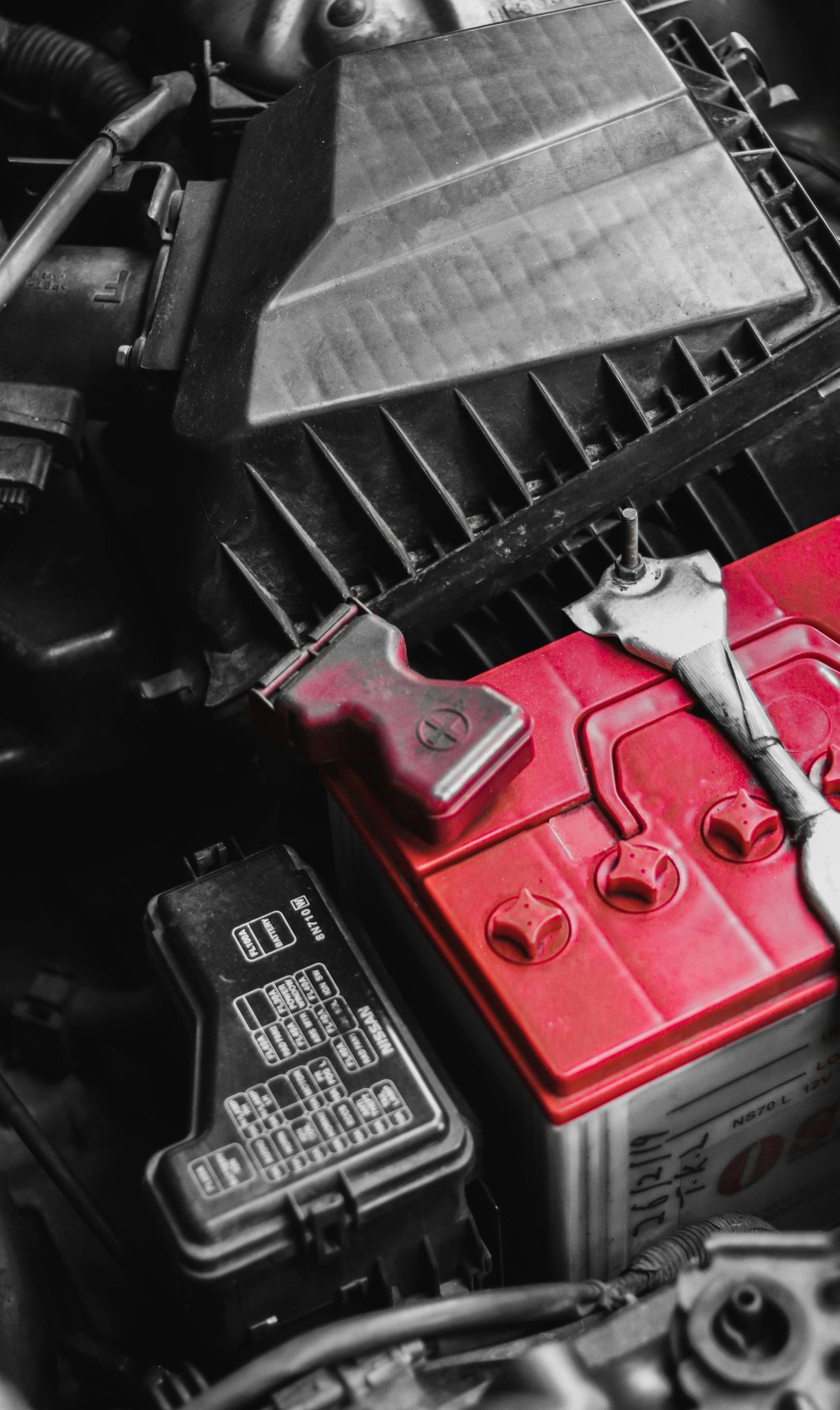 A red battery is sitting under the hood of a car.