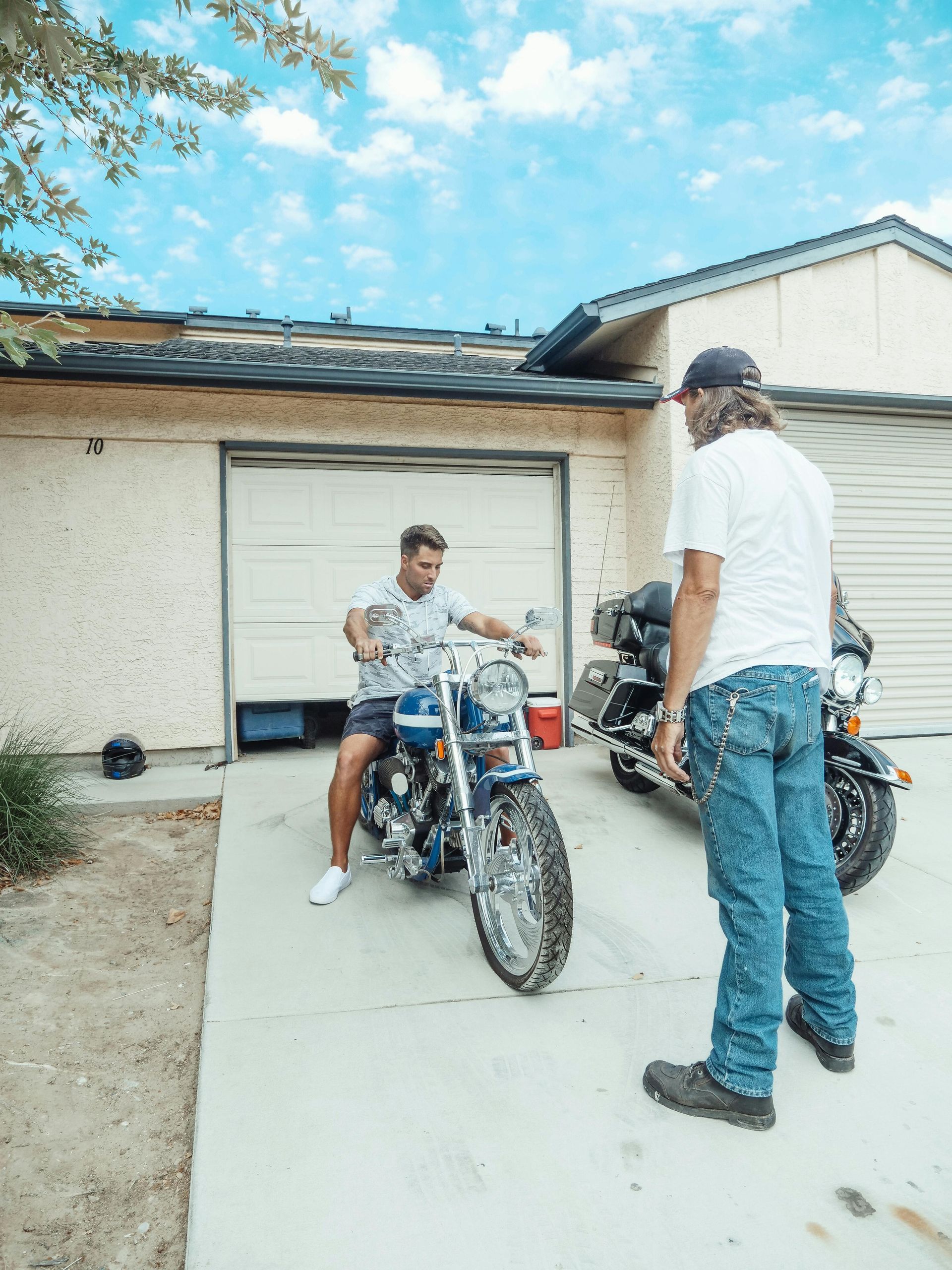 A man is standing next to a man on a motorcycle in front of a house.