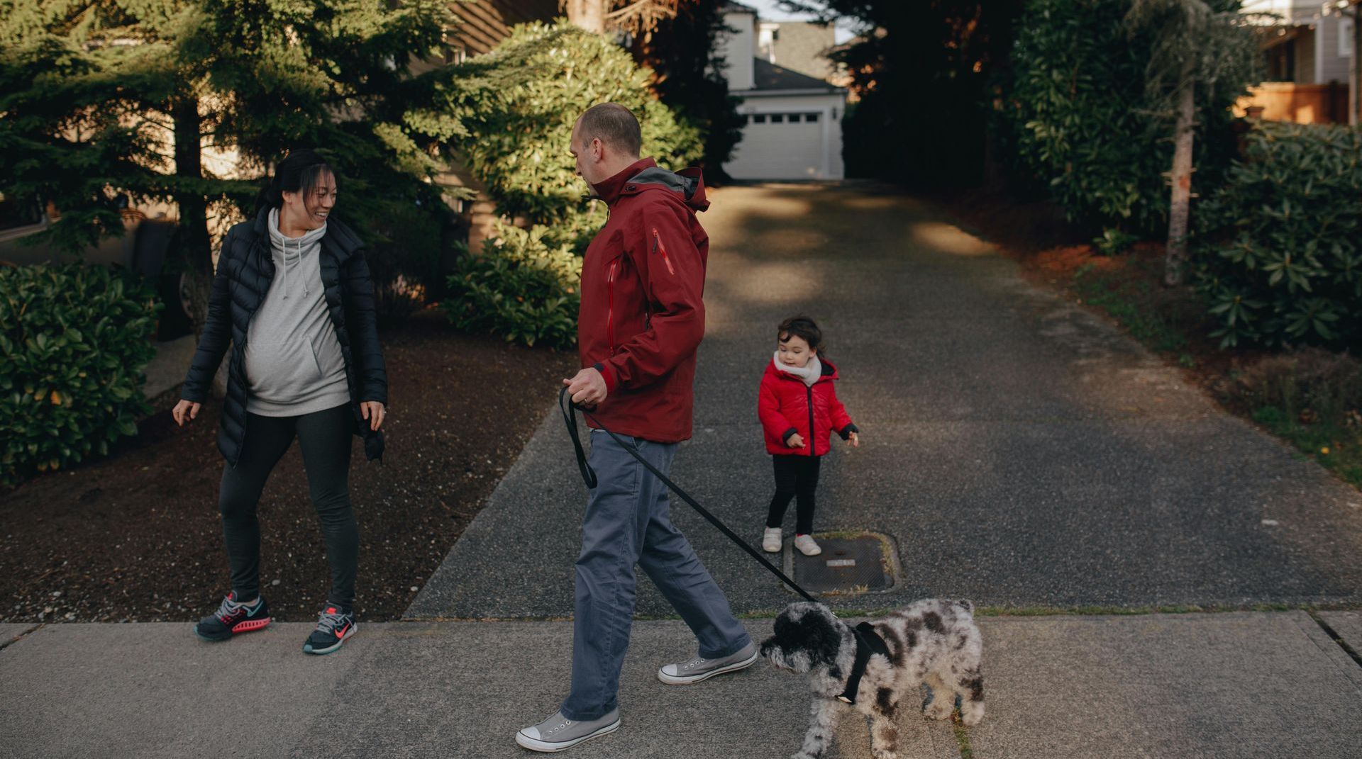 A man is walking a dog on a leash next to a woman and a child.