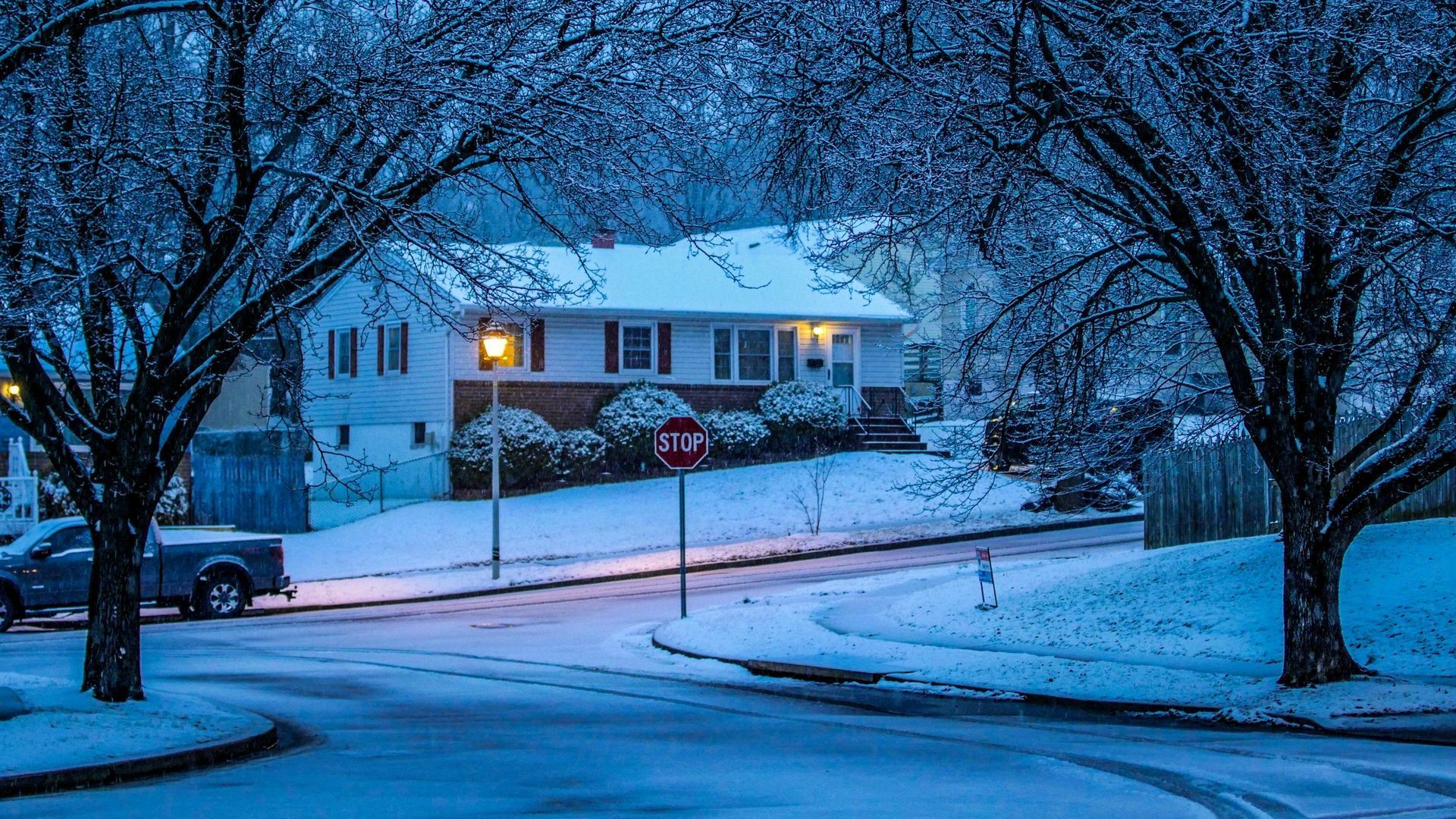 A stop sign is in the middle of a snowy street in front of a house.