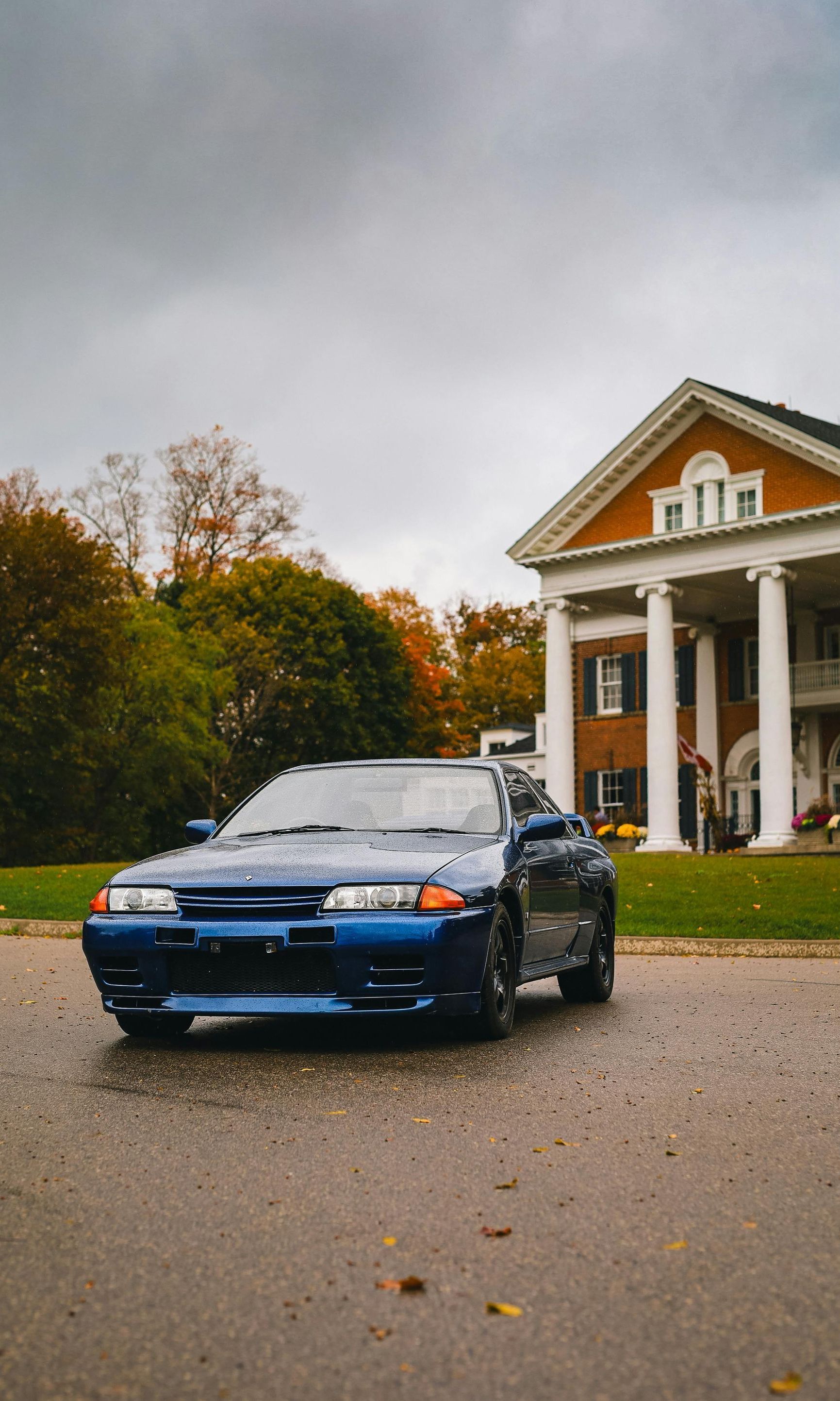 A blue car is parked in front of a large house.