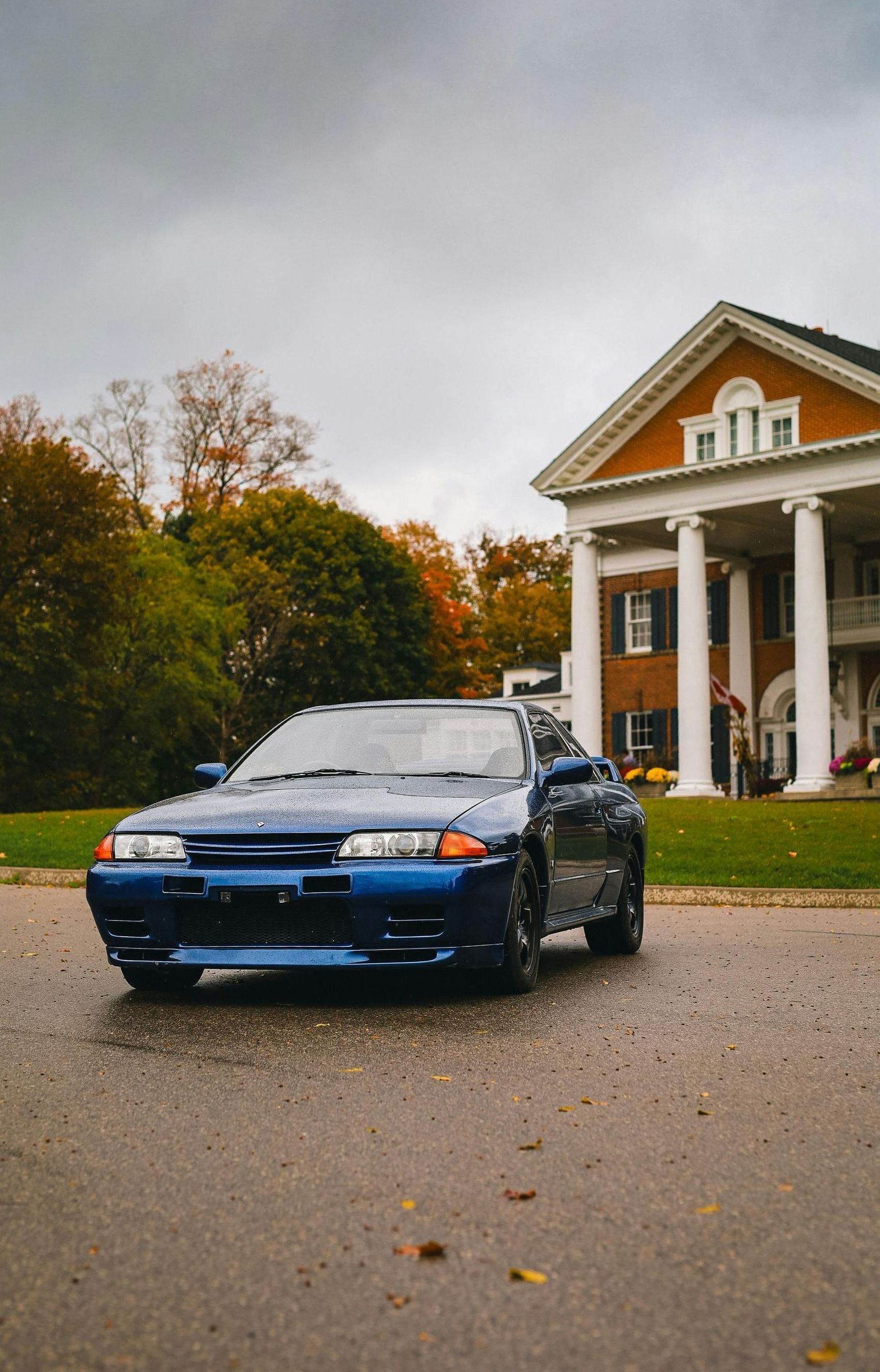 A blue car is parked in front of a large house.