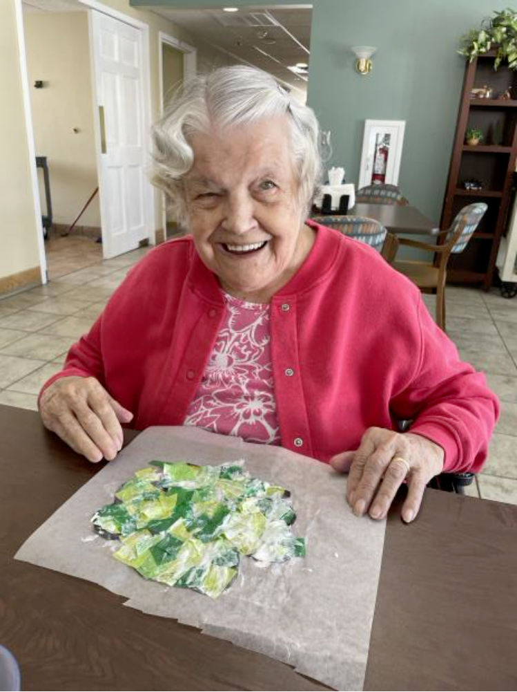 An elderly woman is sitting at a table with a painting on it.