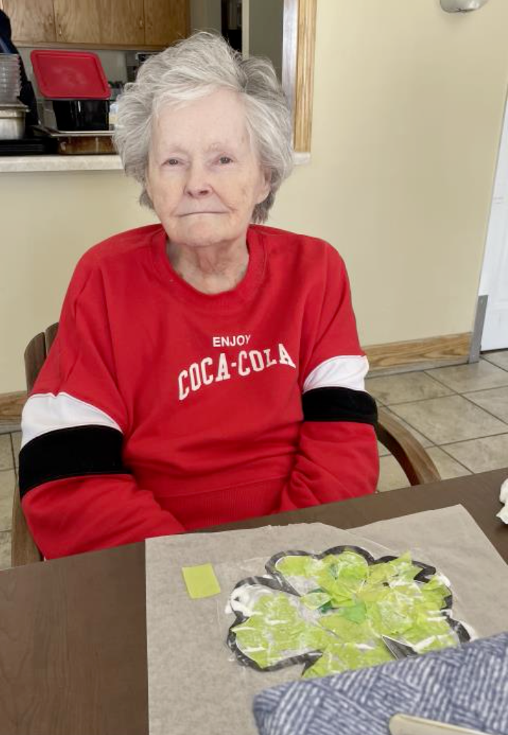 An elderly woman wearing a red coca cola sweatshirt sits at a table