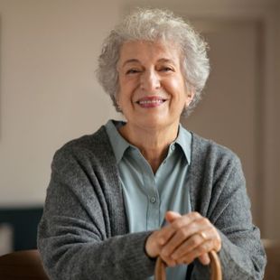 An elderly woman is smiling and holding a cane.