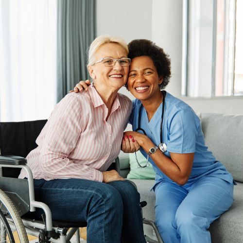 A nurse is sitting next to a woman in a wheelchair on a couch.