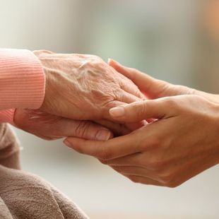 A woman is holding the hand of an older woman.