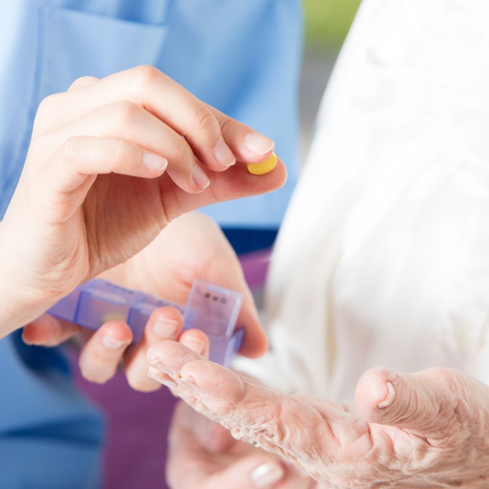 A nurse is giving an elderly woman a pill from a pill box.