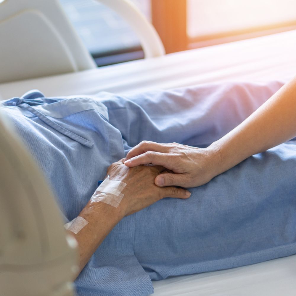 A woman is holding the hand of a patient in a hospital bed.