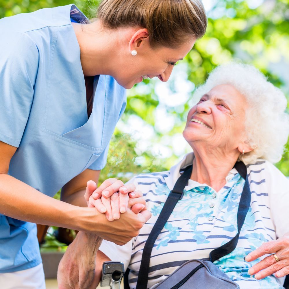 A nurse is holding the hand of an elderly woman in a wheelchair.