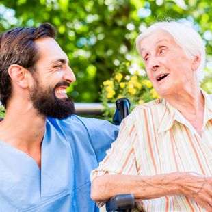 A man with a beard is talking to an elderly woman in a wheelchair.