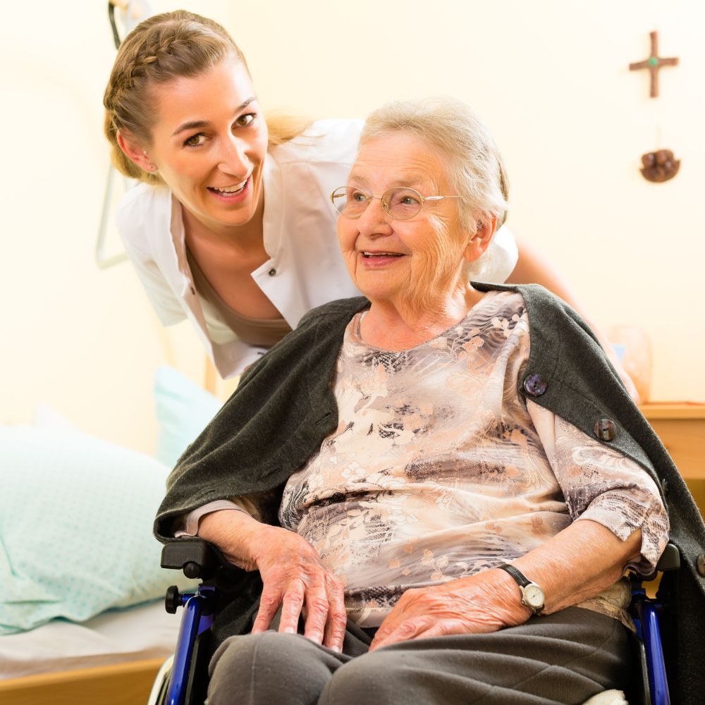 An elderly woman in a wheelchair is being helped by a nurse