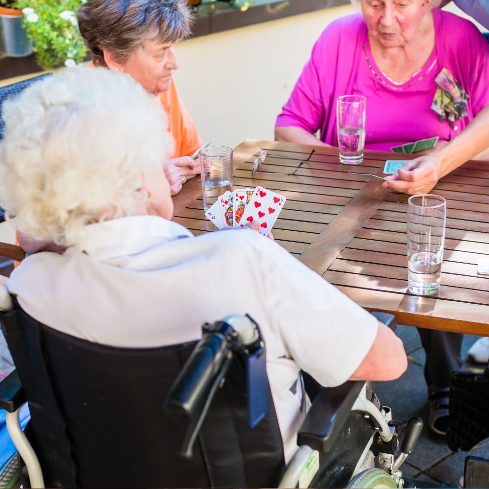 A woman in a wheelchair is playing cards with two other women