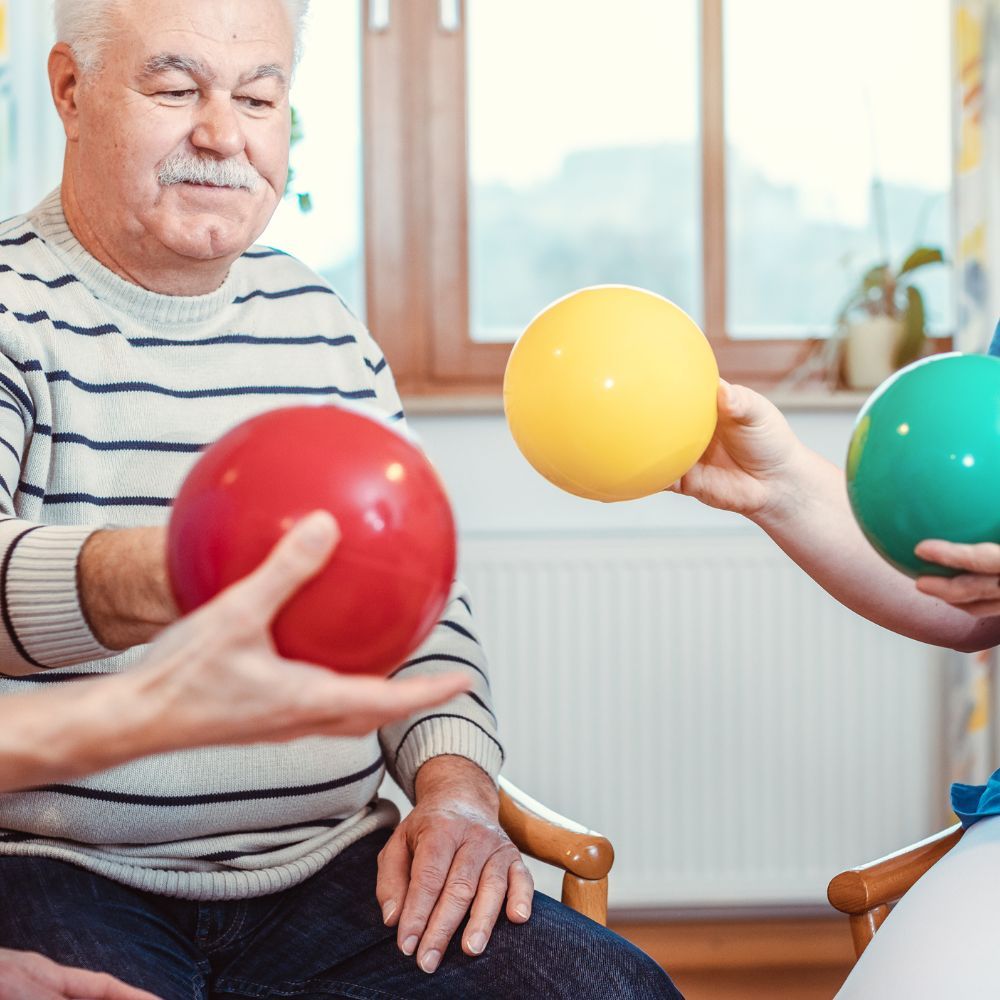 A man is sitting in a chair holding a red ball and a yellow ball