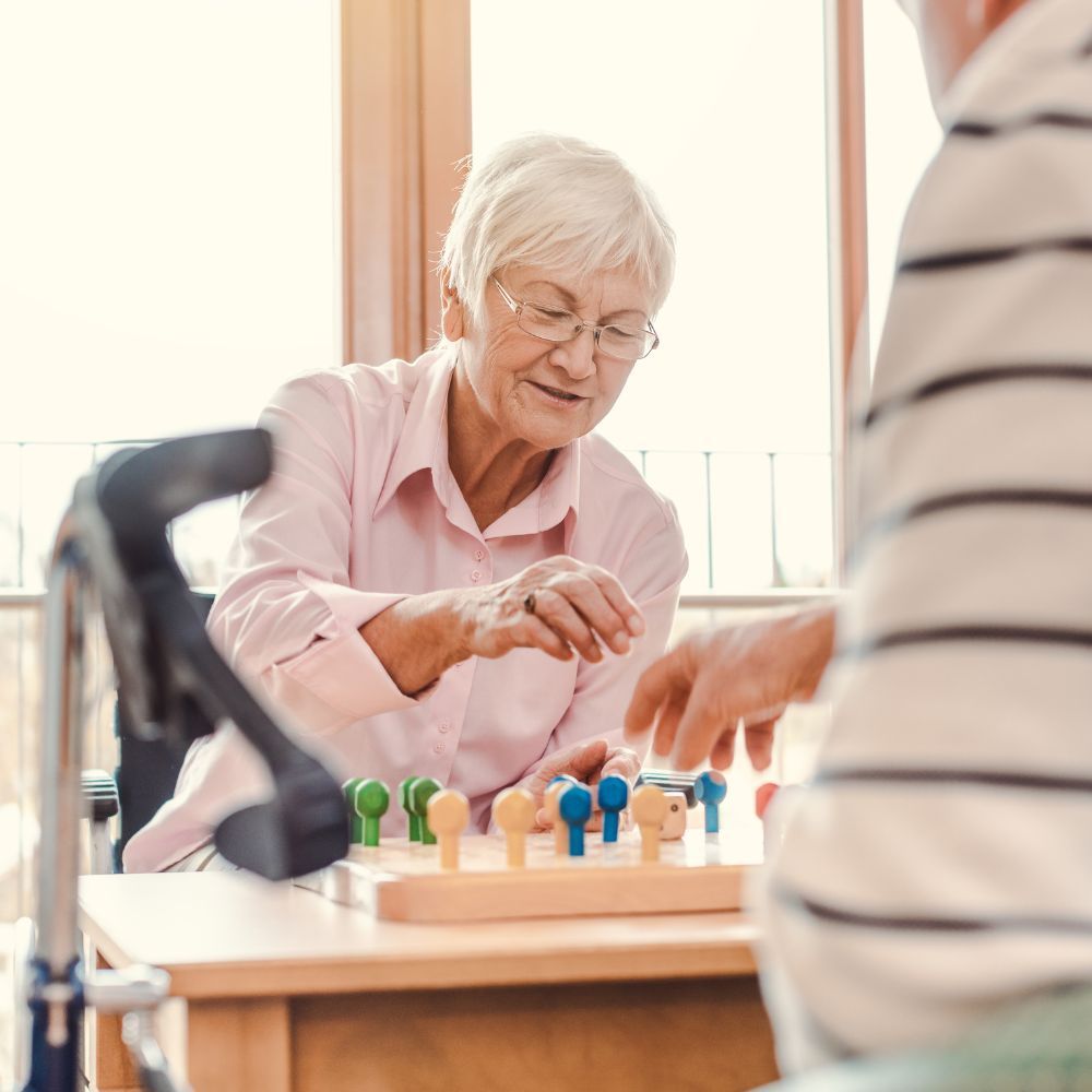 An elderly woman is sitting at a table playing a game with a man.