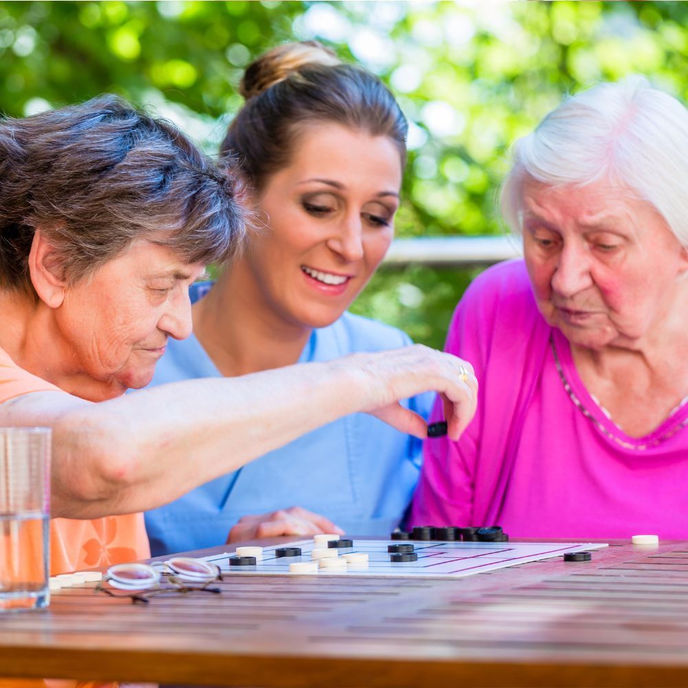 Three women are sitting at a table playing a game of checkers.