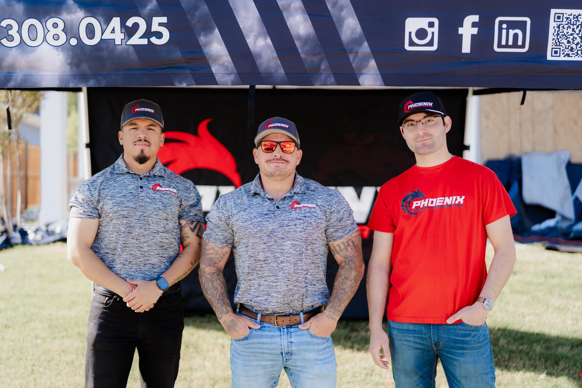 Three men in front of a banner. Two in grey shirts, one in red. All wearing caps, smiling.