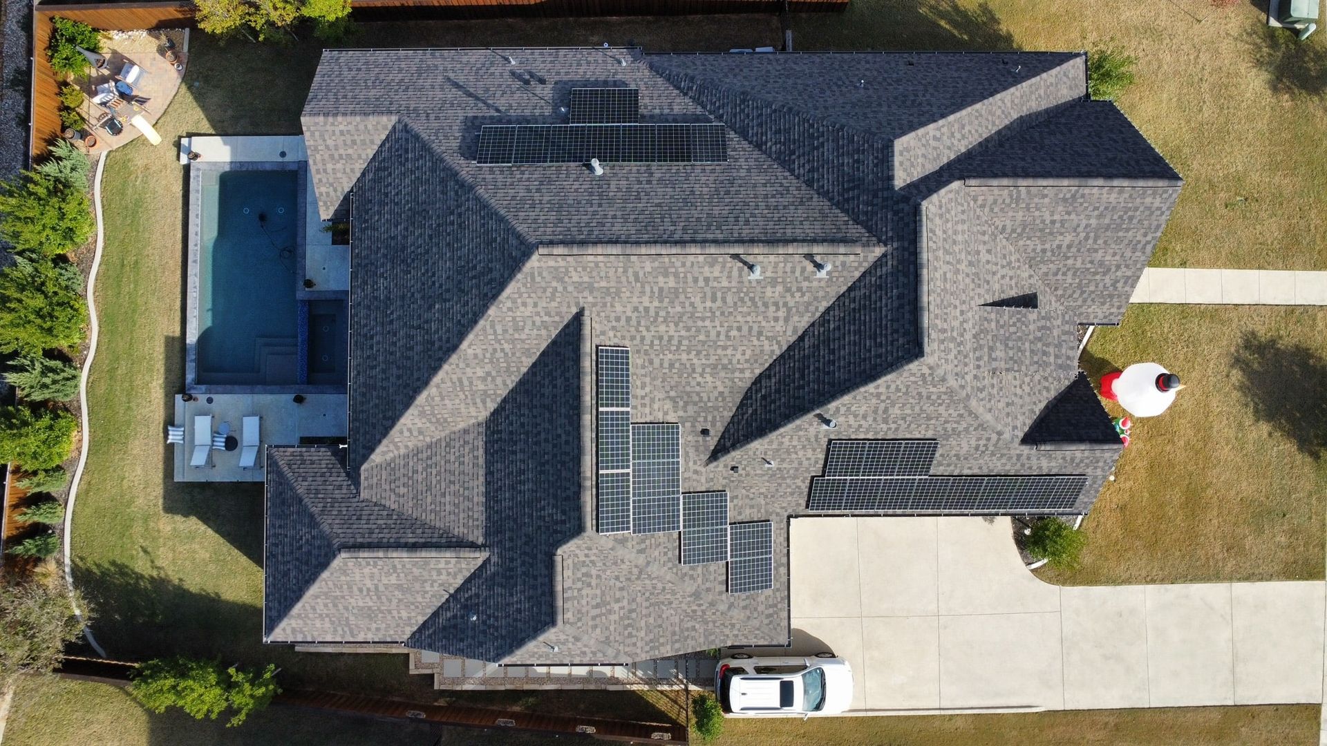 Overhead view of a house with gray roof, solar panels, pool, and a white car in the driveway.