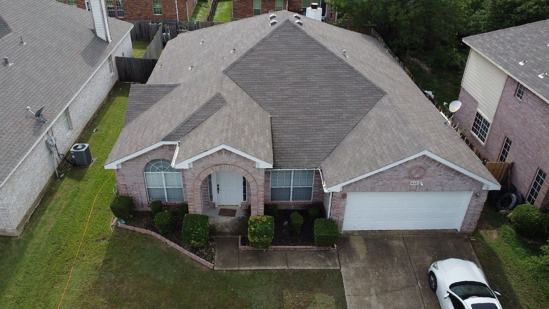 Brick house with gray roof and attached garage. A car sits in the driveway.