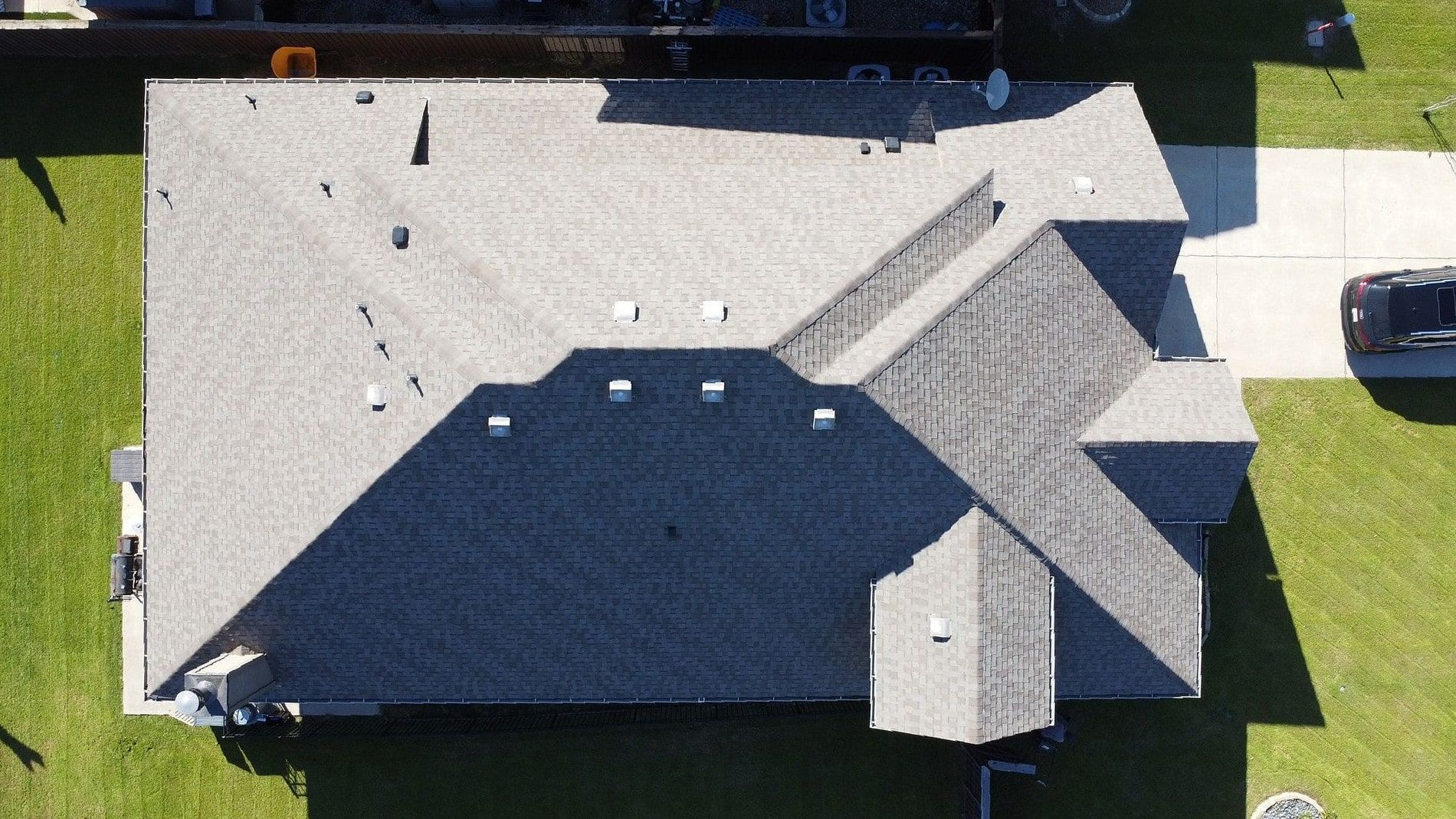 Overhead view of a house with a gray roof, a driveway, and green grass.