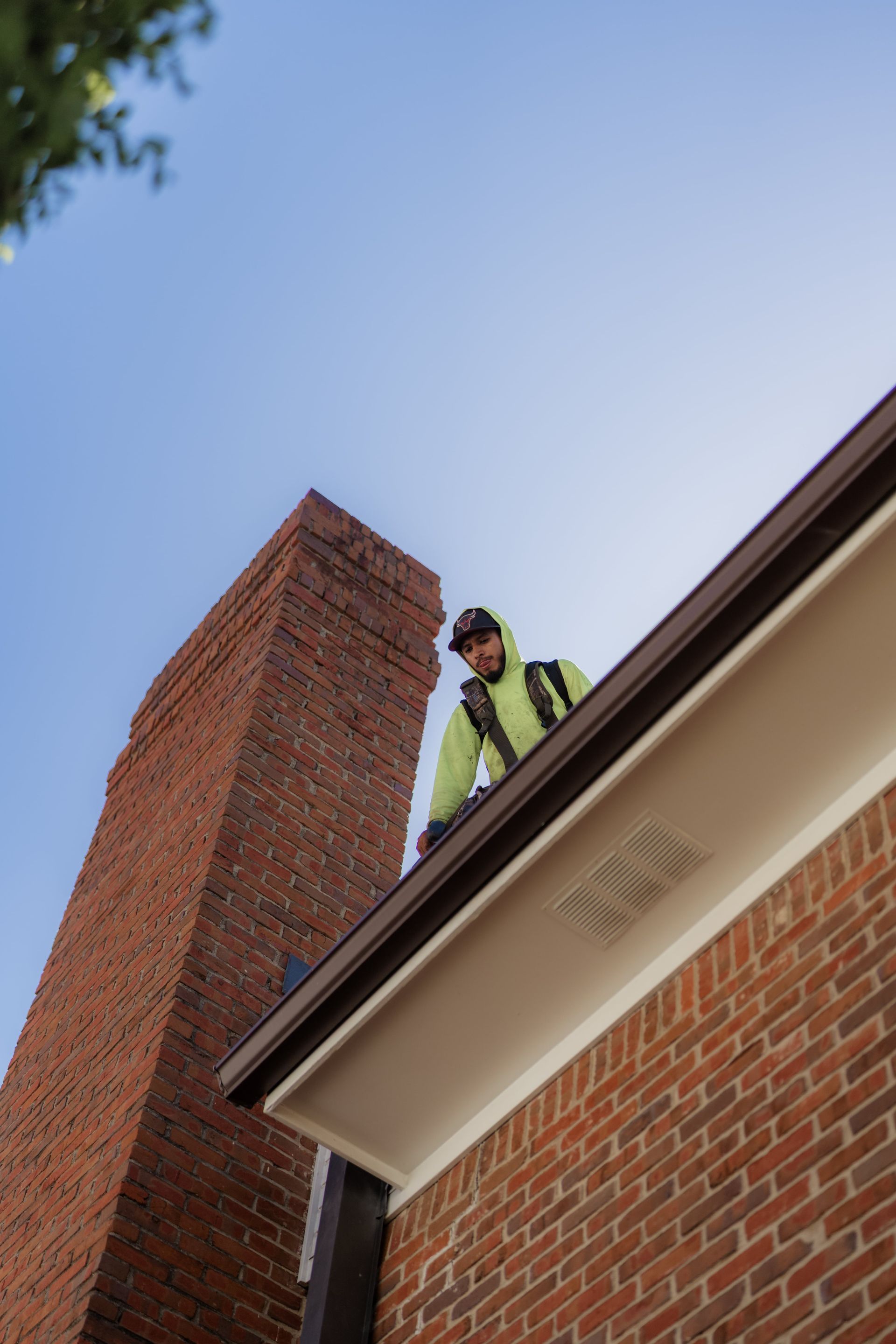 Man on a roof with a brick chimney and clear sky.