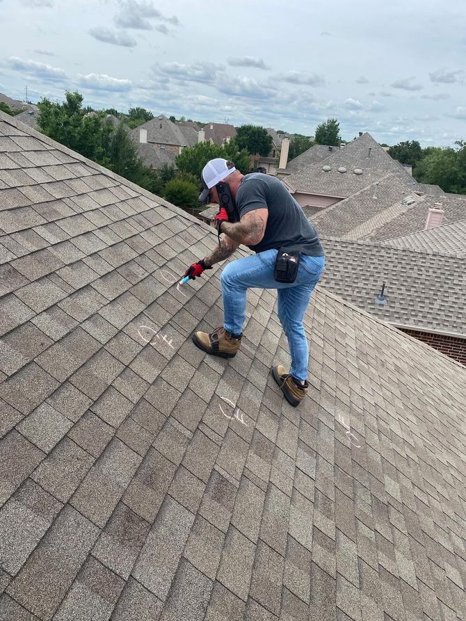 Emergency Roof Inspections - Phoenix Storm Restoration Man on a rooftop with tools, assessing shingles. Wearing safety gear and jeans. Houses in the background.