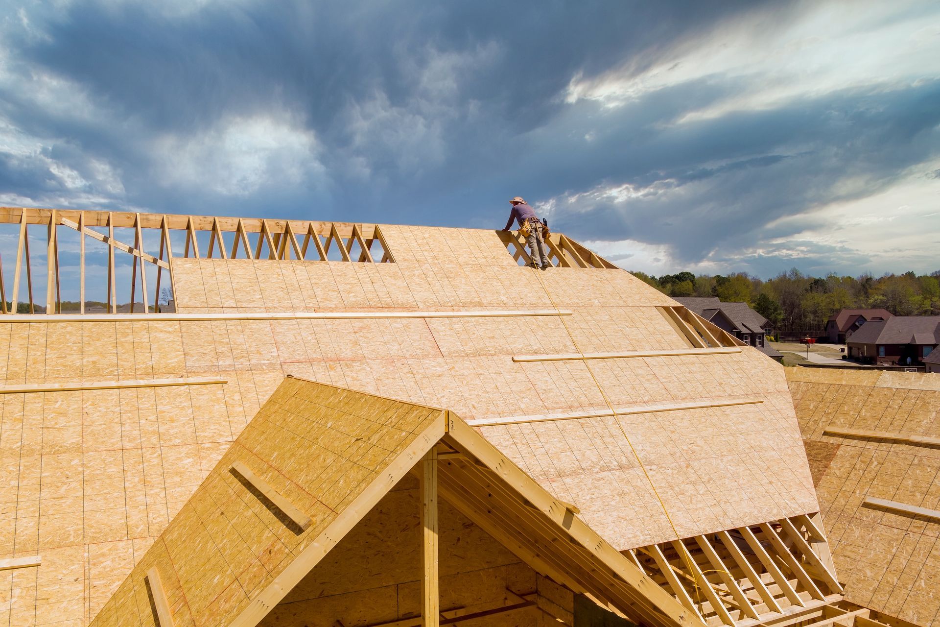 Construction workers installing plywood sheathing on a roof under a cloudy sky.