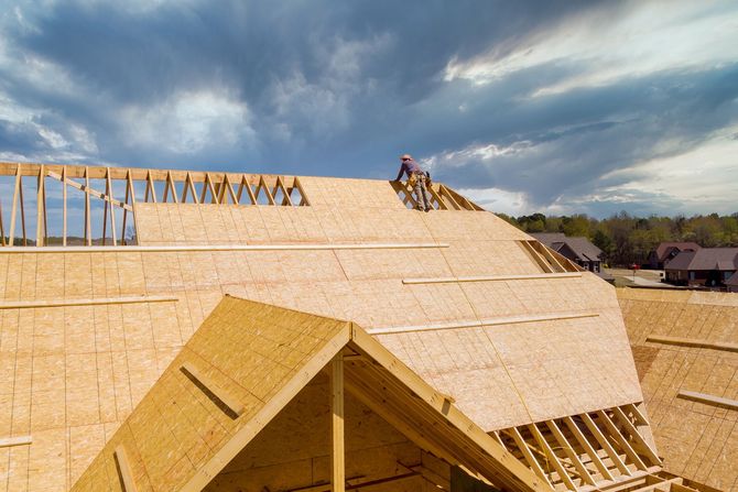 New Roof Installation - Phoenix Storm Restoration Construction workers installing plywood sheathing on a roof under a cloudy sky.
