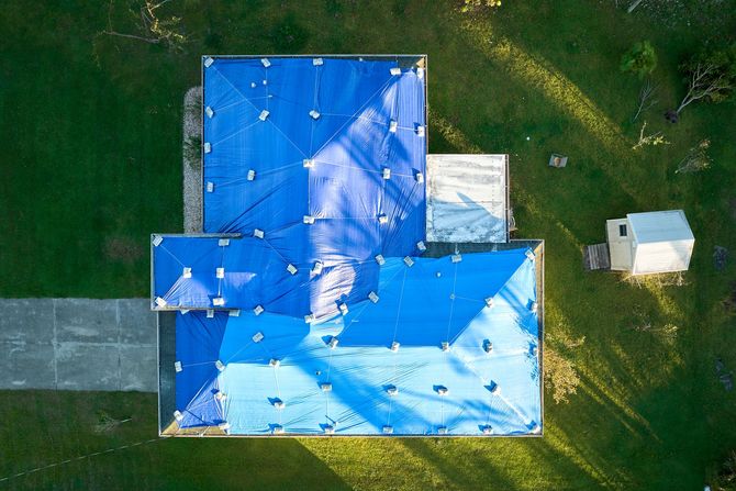 Emergency Tarping - Phoenix Storm Restoration Overhead view of building with blue tarp roof, surrounded by green grass and a small white structure.